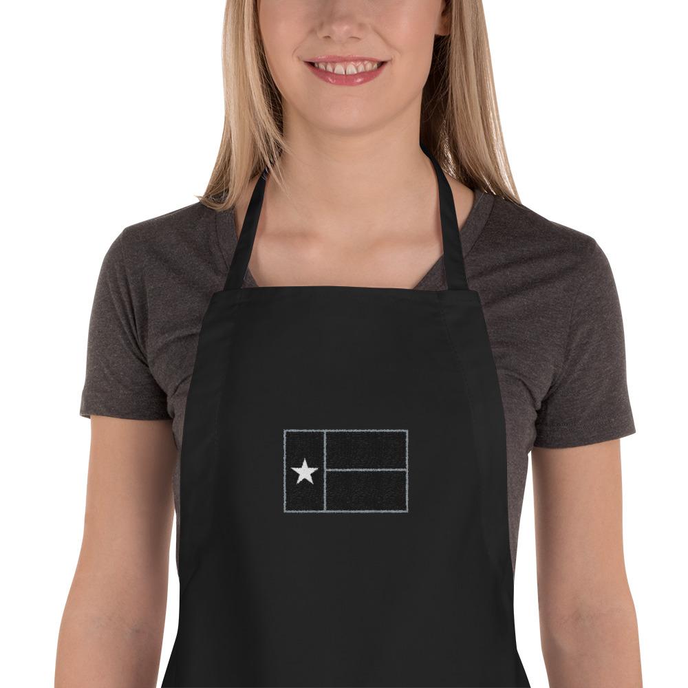 Blonde woman wearing black apron with black Texas flag
